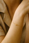 Gold bracelet with a heart charm on a person's wrist against a neutral background