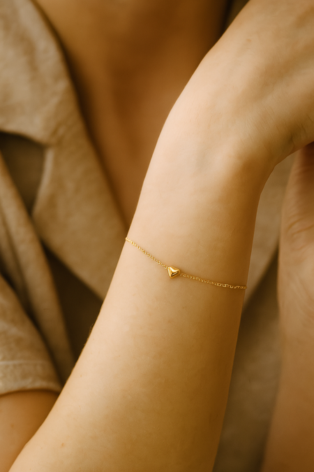 Gold bracelet with a heart charm on a person's wrist against a neutral background