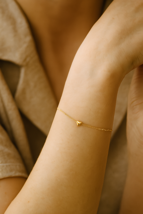 Gold bracelet with a heart charm on a person's wrist against a neutral background