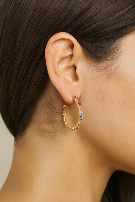 Close-up of an ear wearing a gold hoop earring with colorful stones.