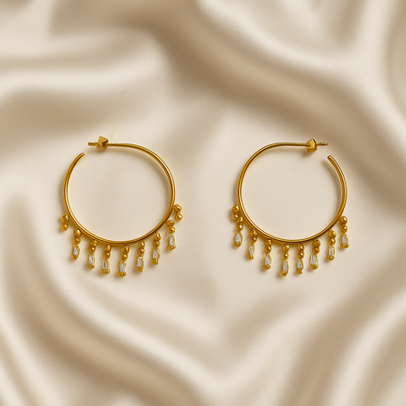 Gold hoop earrings with dangling beads on a beige fabric background