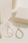 Silver teardrop earrings on a white surface with a soft background