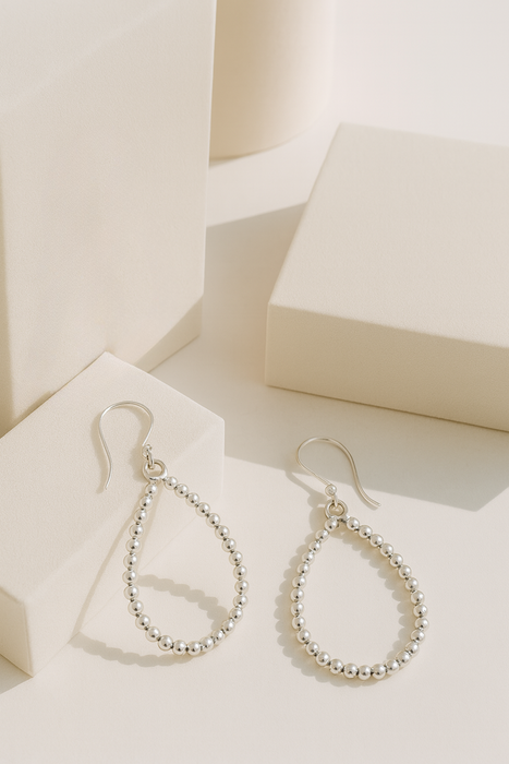Silver teardrop earrings on a white surface with a soft background