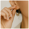 Gold hoop earring being worn with a hand adjusting it.